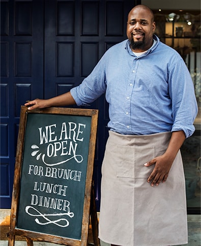 A smiling restaurant owner standing beside a “We are open” chalkboard