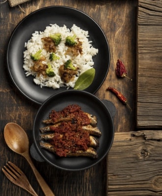 Rice with vegetables and spiced fried fish served on a rustic wooden table